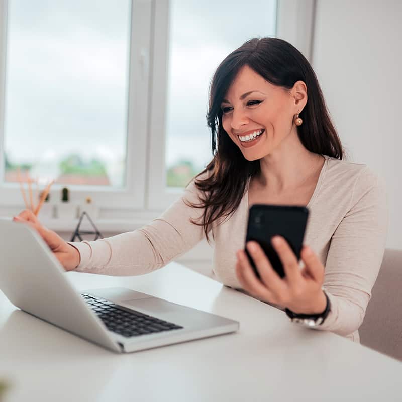 Portrait of a successful smiling woman using the Invoice 4 Business accounting app on her laptop and mobile phone.